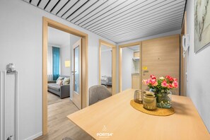 A modern hotel room with a wooden dining table, a vase of flowers, and a view of the living area. - "Holiday Apartment Sylt" in the heart of Büsum with balcony, close to the beach (Büsum)