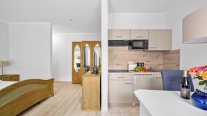 Ein kleines Hotelzimmer mit Bett, Holzschrank, einer Küchenzeile inklusive Mikrowelle, Spüle und einer Essecke.