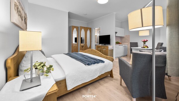 Ein modernes Hotelzimmer mit einem hölzernen Bett, einem Schreibtisch mit Lampe, einem Sessel und einem Fernseher.