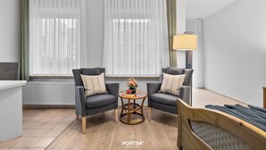 Ein modernes Wohnzimmer mit zwei grauen Sesseln, einem Holztisch mit Blumenvase und einem Bett mit Decke.