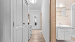 Ein Flur mit Holzboden, weißen Wänden und einem Badezimmer mit Waschbecken und Spiegel.