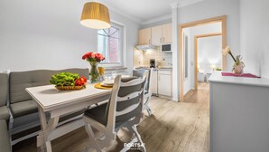 Eine moderne Küche mit weißen Schränken, ein Essbereich mit weißem Tisch und Stühlen sowie ein graues Sofa.