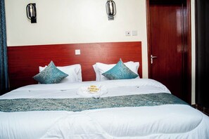 A hotel room with a wooden headboard, a bed with white bedding and blue patterned pillows, and a matching throw blanket. - Fantastic 3-bedroom apartment with AC in vibrant Mombasa (Mombasa)
