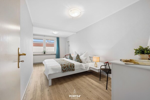 A bedroom with a bed, bedside table, chair, and a window with curtains. - "Ferienwohnung Muschel" in the heart of Büsum with balcony, center and close to the beach (Büsum)