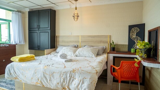 Un dormitorio con cama, escritorio, silla, armario y lámpara colgante.