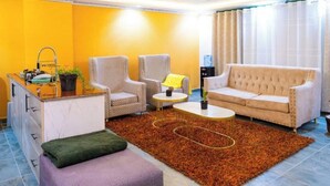 Un espacio habitable compacto con sofá, dos sillones, una mesa de centro, una pequeña cocina con fregadero y una planta en maceta.
