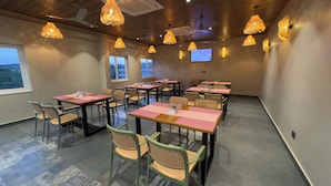 A conference room with tables and chairs, ceiling fans, and hanging lights. - MALPE RIVIERA (Udupi)