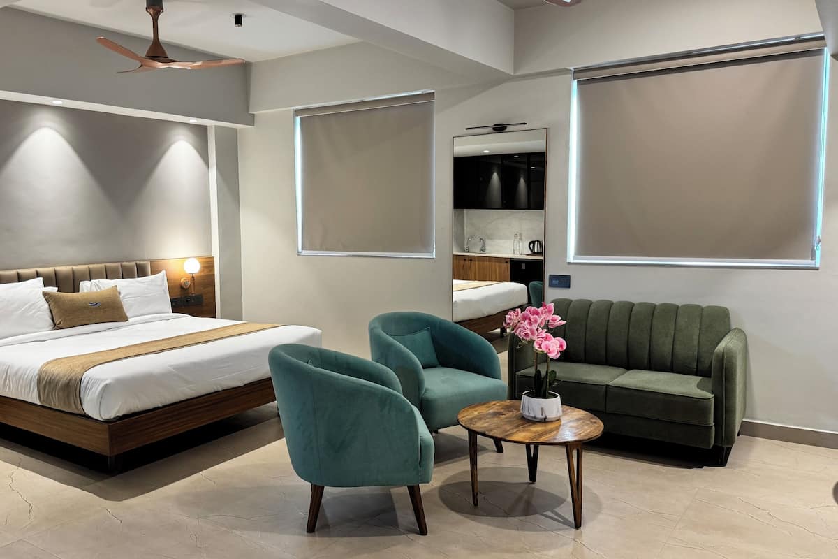 A modern hotel room with a large bed, two armchairs, a small round table, and a sofa.