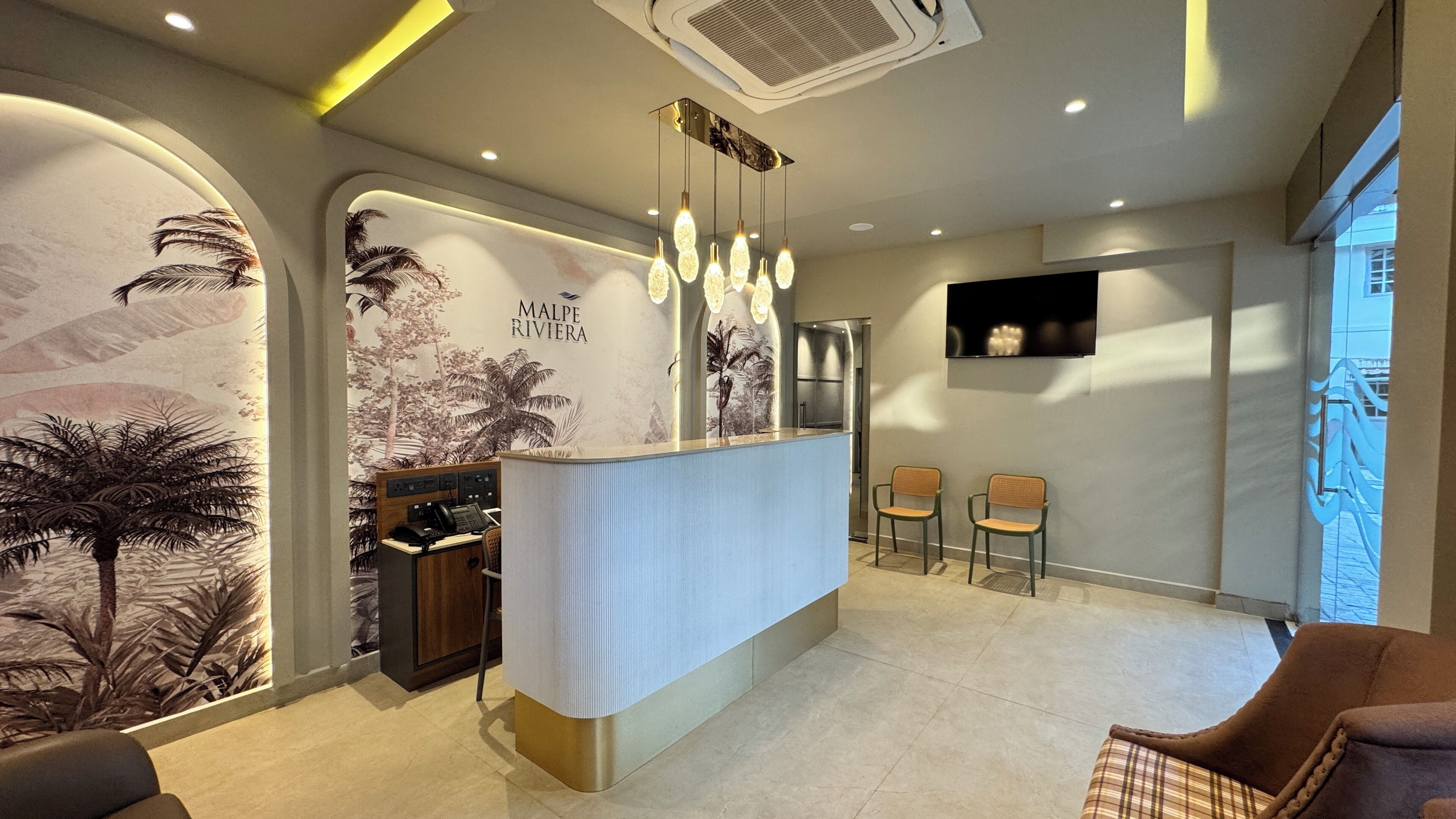 A reception area with a counter, two chairs, a wall-mounted TV, and a ceiling air vent.