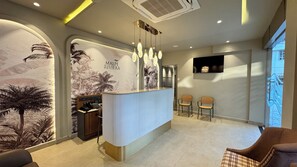 A reception area with a counter, two chairs, a wall-mounted TV, and a ceiling air vent.