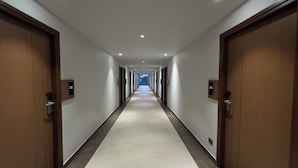 A long, narrow hallway with doors on both sides, each with a digital display showing room numbers. - MALPE RIVIERA (Udupi)