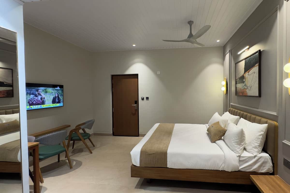 A modern hotel room with a large bed, a TV mounted on the wall, a ceiling fan, and a door leading to another room.