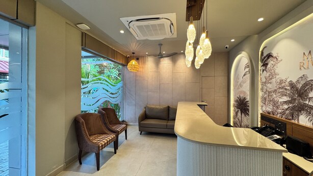 A reception area with a curved counter, two leather chairs, a ceiling fan, and a wall mural. - MALPE RIVIERA (Udupi)