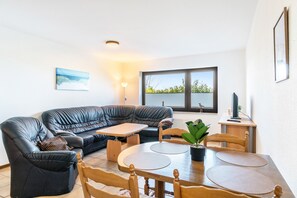 A living room with a sectional sofa, a dining table with chairs, a potted plant, and a television. - Apartment '3' with Private Terrace, Shared Garden and Wi-Fi (Horumersiel-Schillig)