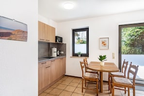 A compact kitchen with wooden cabinets, a microwave, and a dining table with chairs. - Apartment 2 with Private Terrace, Shared Garden and Wi-Fi (Horumersiel-Schillig)
