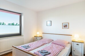 Un dormitorio con cama, dos mesitas de noche, una ventana con persianas y un radiador.