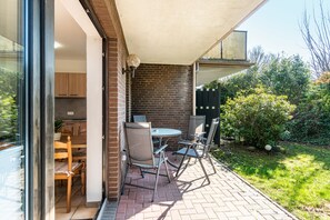Un patio con una mesa y sillas, un muro de ladrillo y una puerta de cristal que da a una habitación con muebles de madera.
