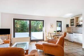 Ein Wohnzimmer mit Fernseher, orangefarbenen Sofas, einem Glastisch und einer Glasschiebetür, die auf einen Balkon führt.