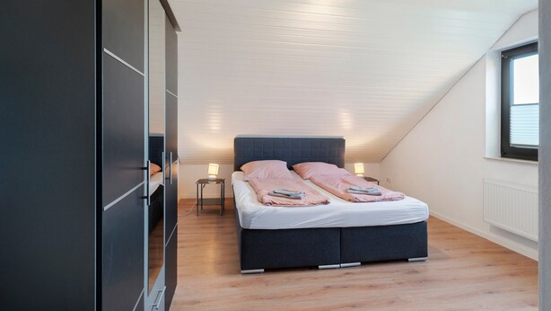 Un dormitorio con cama, mesitas de noche, un armario y una ventana.