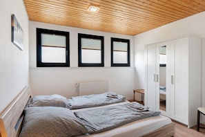 Ein Schlafzimmer mit zwei Betten, einem Kleiderschrank und drei Fenstern.