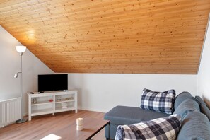 Ein Wohnzimmer mit Holzboden, einem Fernseher auf einem weißen Schrank, einem blauen Sofa und einer Stehlampe.