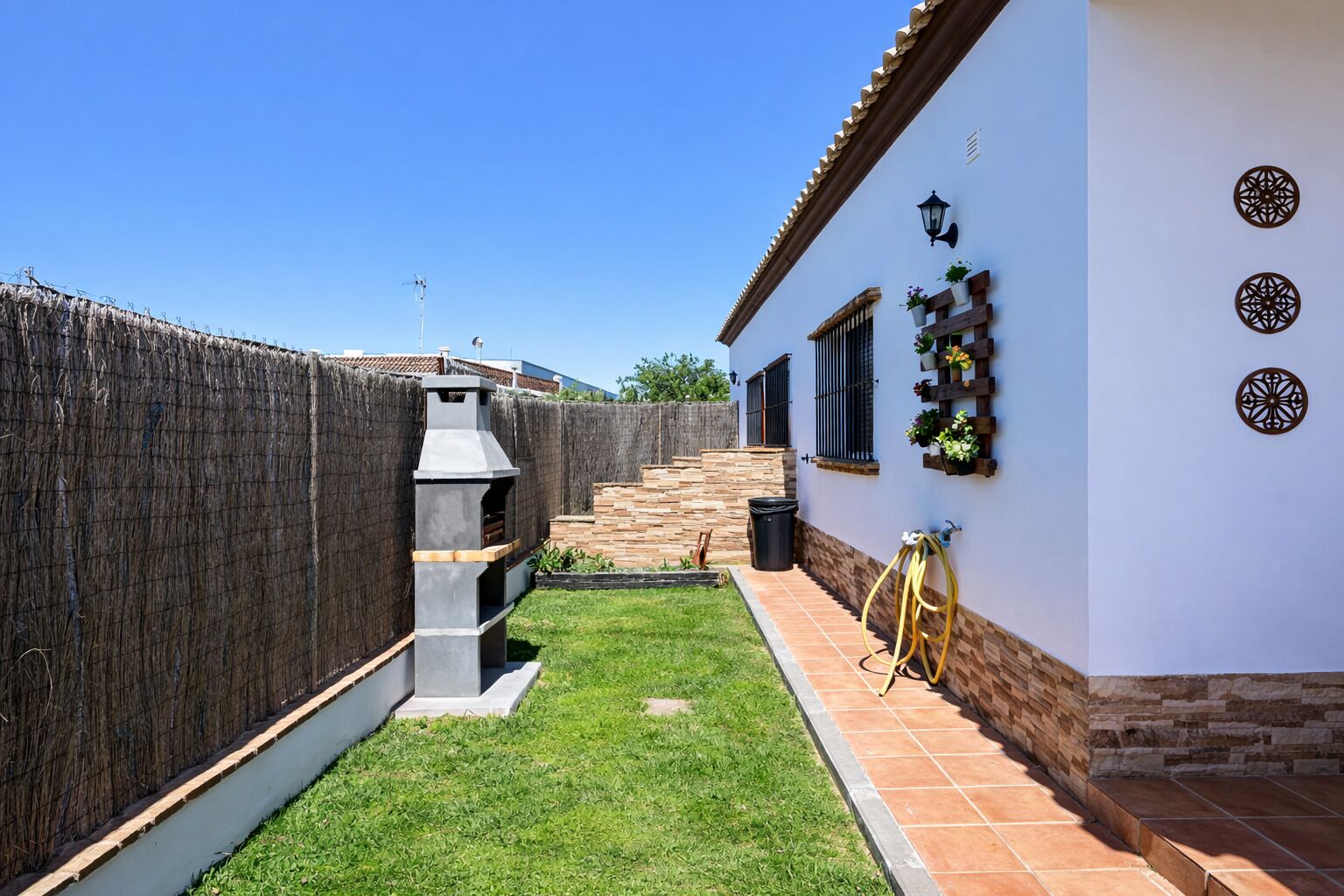 A backyard with a barbecue grill, a wooden fence, and a house with a tiled patio.