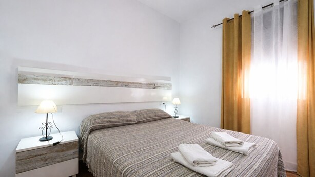 Ein Hotelzimmer mit einem Bett, zwei Nachttischen mit Lampen, einer Kopfteil und einem Fenster mit Vorhängen.