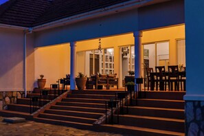 A building with a covered porch, steps leading to a door, and outdoor seating. - Martha's Farm House (Mukono)