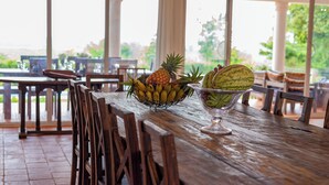 Uma mesa de madeira com uma cesta de frutas contendo bananas, abacaxi e melancia.