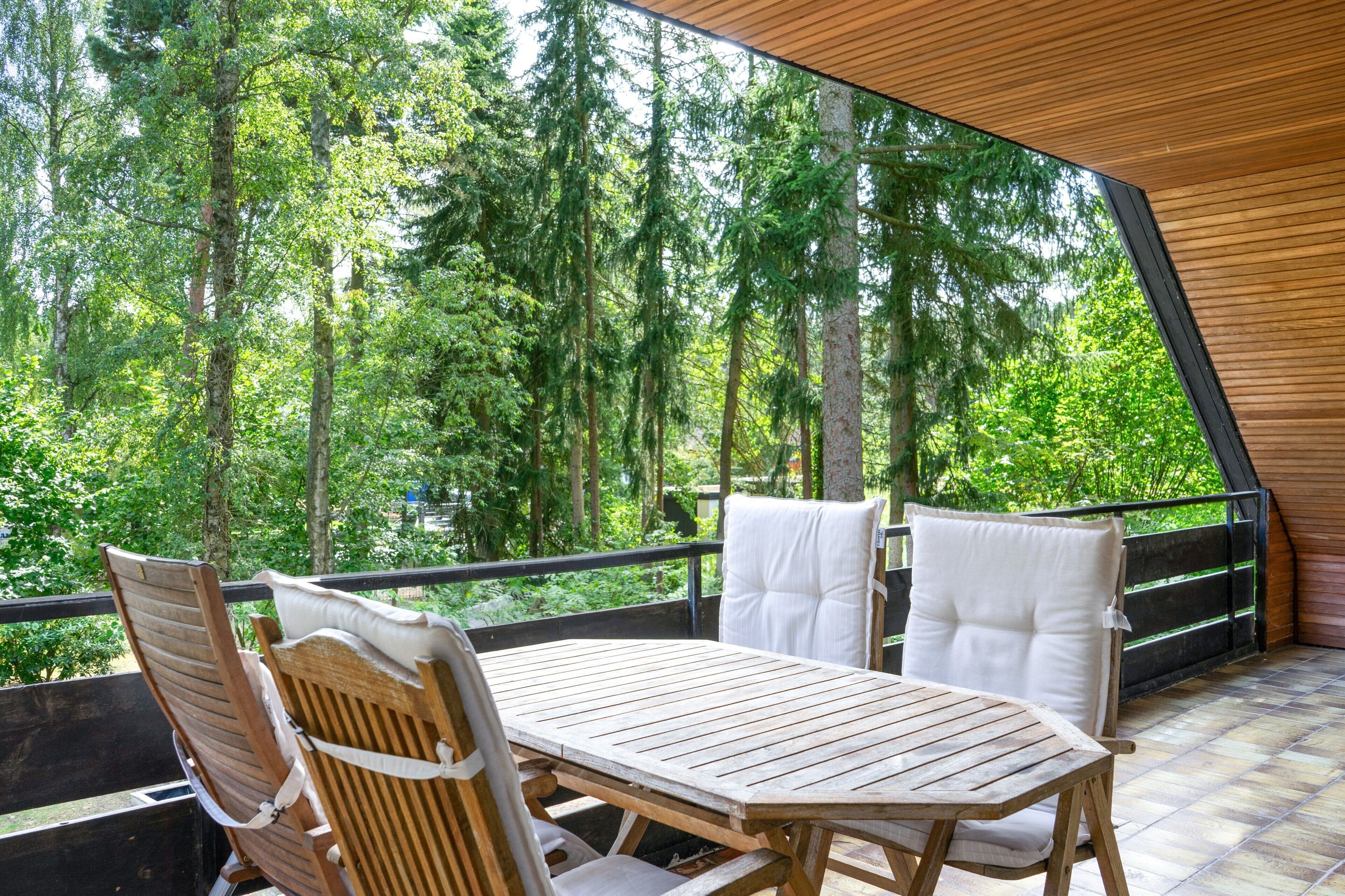 A wooden table and chairs on an outdoor balcony with a view of a forest.