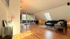 A spacious loft with a high ceiling, a large skylight, a modern sofa, a yellow chair, and a dining area.