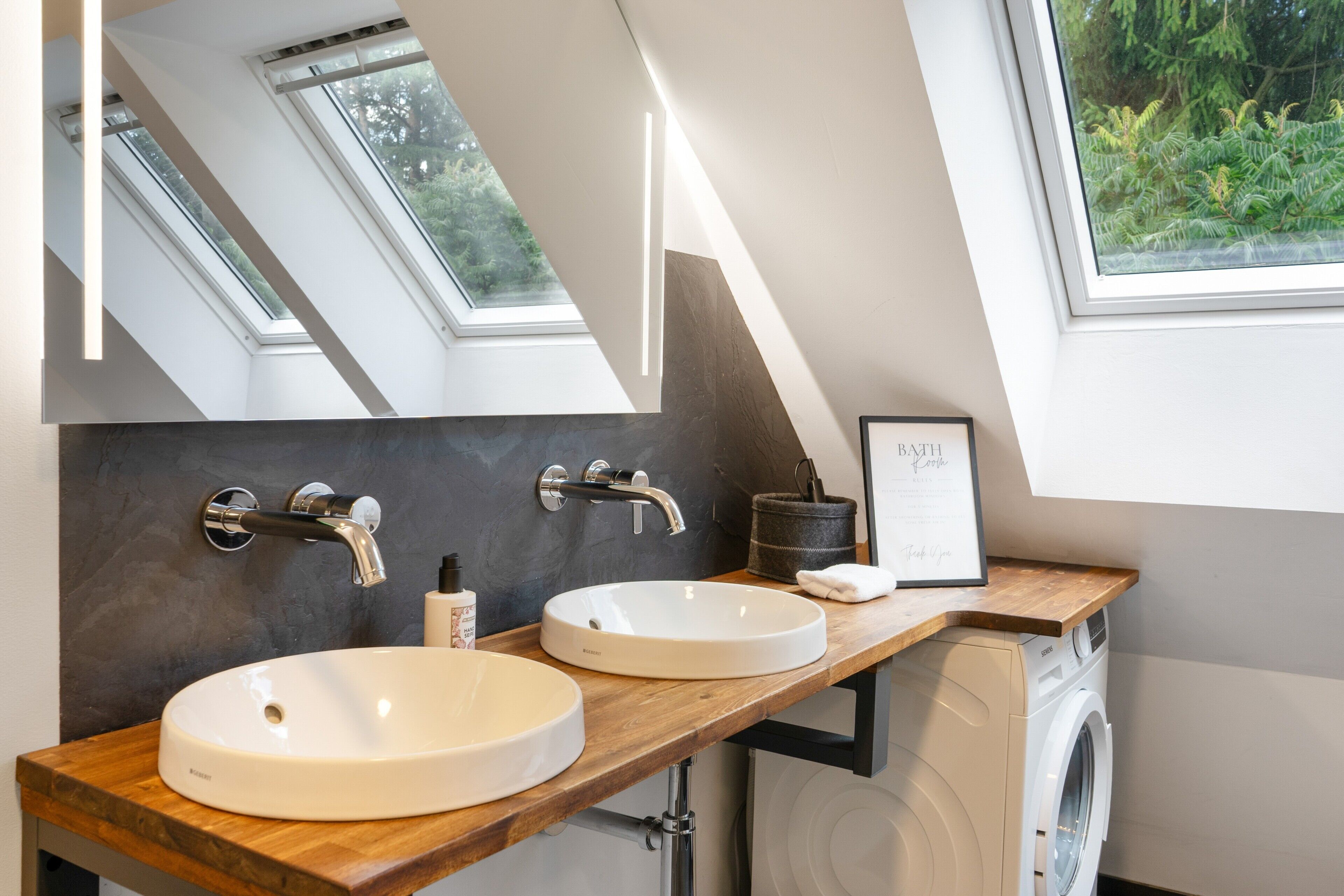 A modern bathroom with skylights, a double sink, and a framed picture on the wall.
