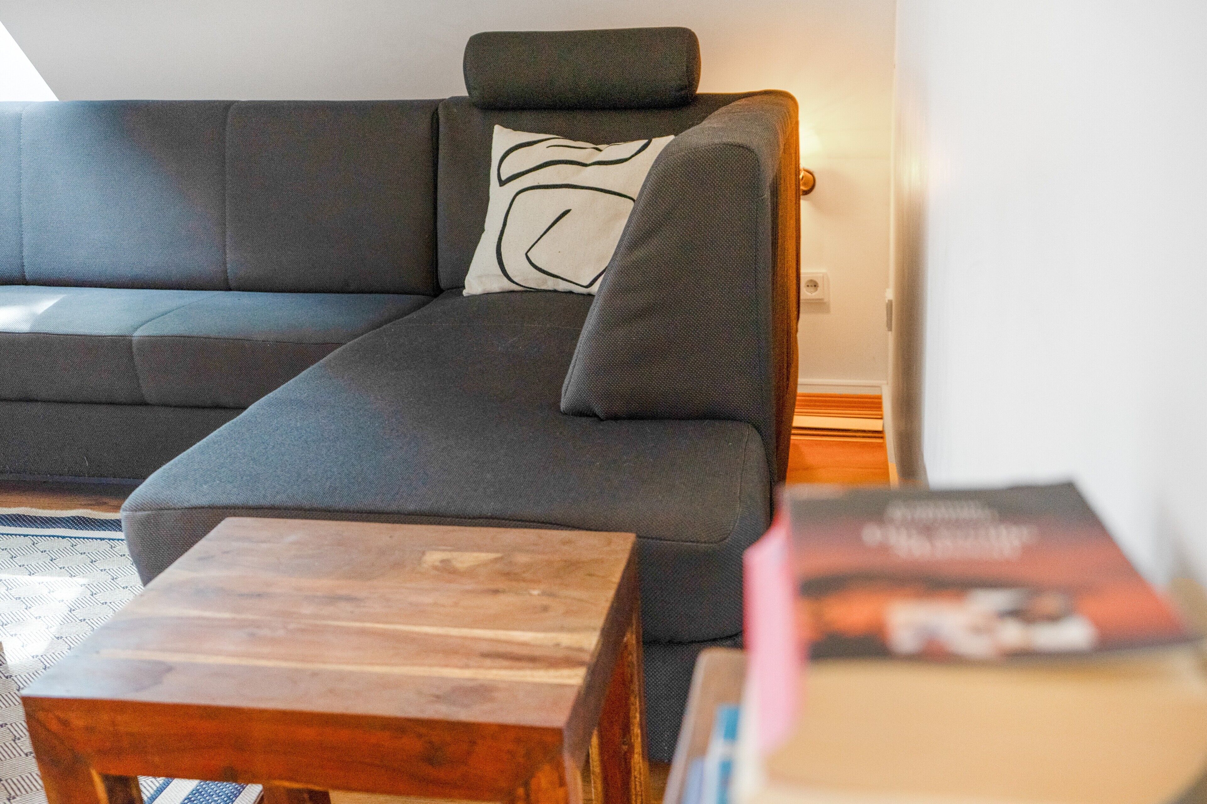 A sectional sofa with a pillow, a wooden coffee table, and a magazine on a table.