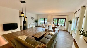 A modern living room with a flat-screen TV, a sofa, a coffee table, and a dining area with chairs and a table.