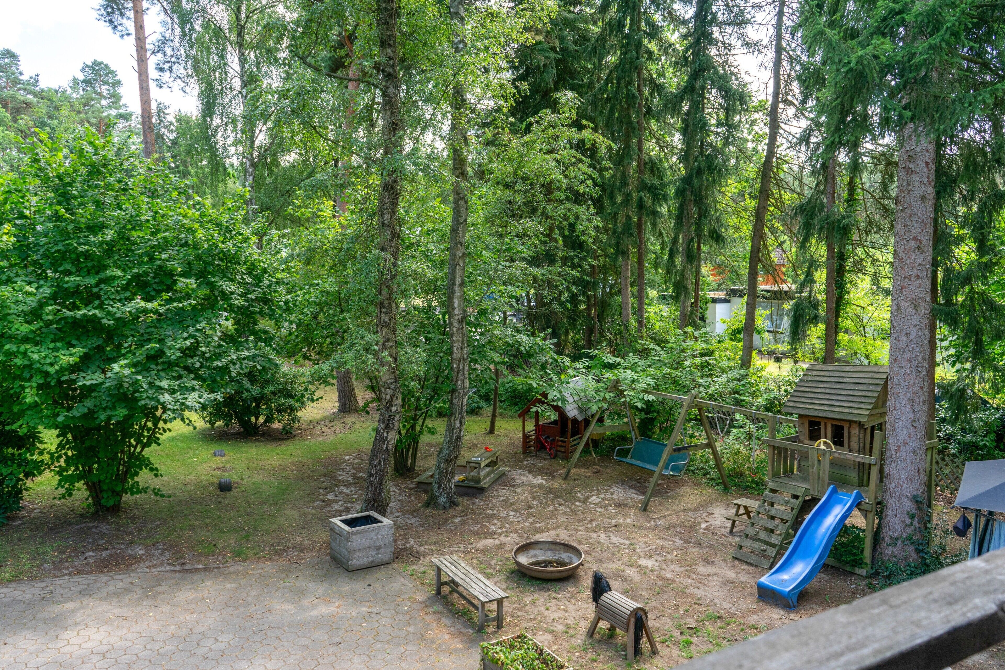 Metsäinen ulkoalue, jossa on leikkipaikka, mukaan lukien liukumäki ja keinut, sekä nuotiopaikka.