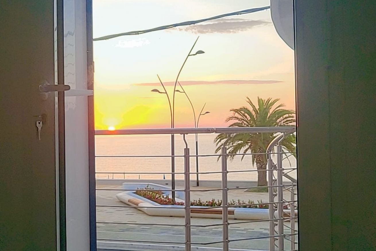 A balcony with a view of the sunset over the sea, a palm tree, and a street lamp.