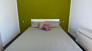 Un lit simple avec une tête de lit blanche, un mur vert et un appareil de climatisation blanc sur le côté droit.