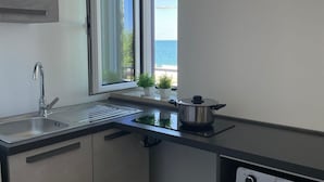 Une cuisine moderne avec un évier en acier inoxydable, une fenêtre donnant sur la mer et une casserole posée sur le plan de travail.