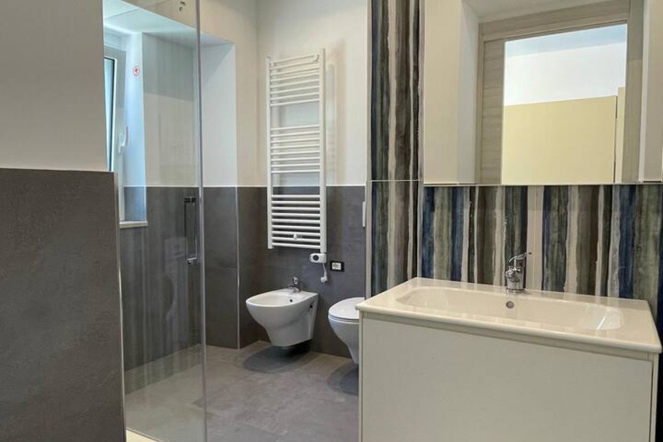 A modern bathroom with a glass shower enclosure, a bidet, a sink, and a mirror.