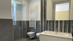 Une salle de bain moderne avec une douche à parois de verre, un bidet, un lavabo et un miroir.