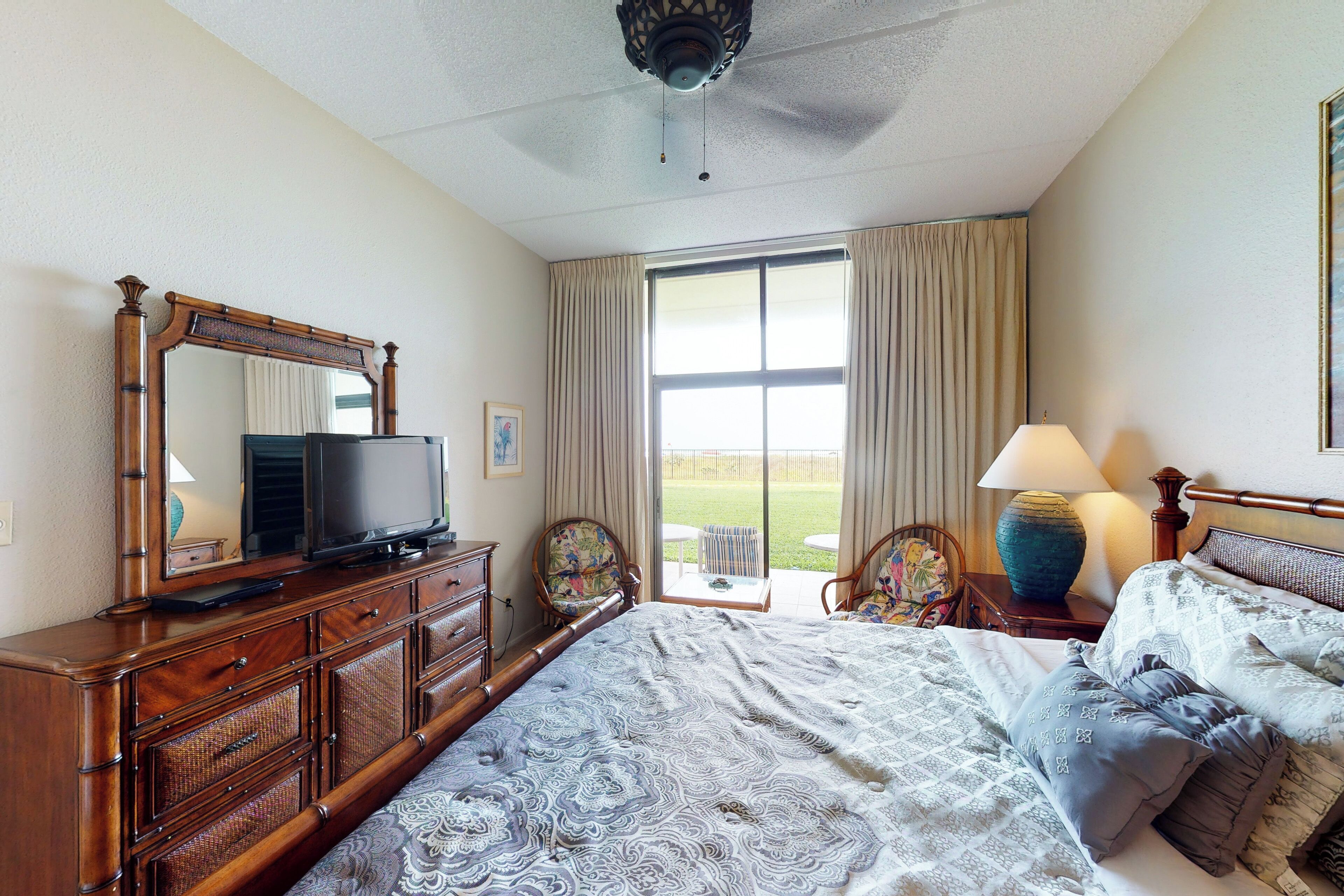 A hotel room with a large bed, a dresser, a television, a chair, and a window with curtains.