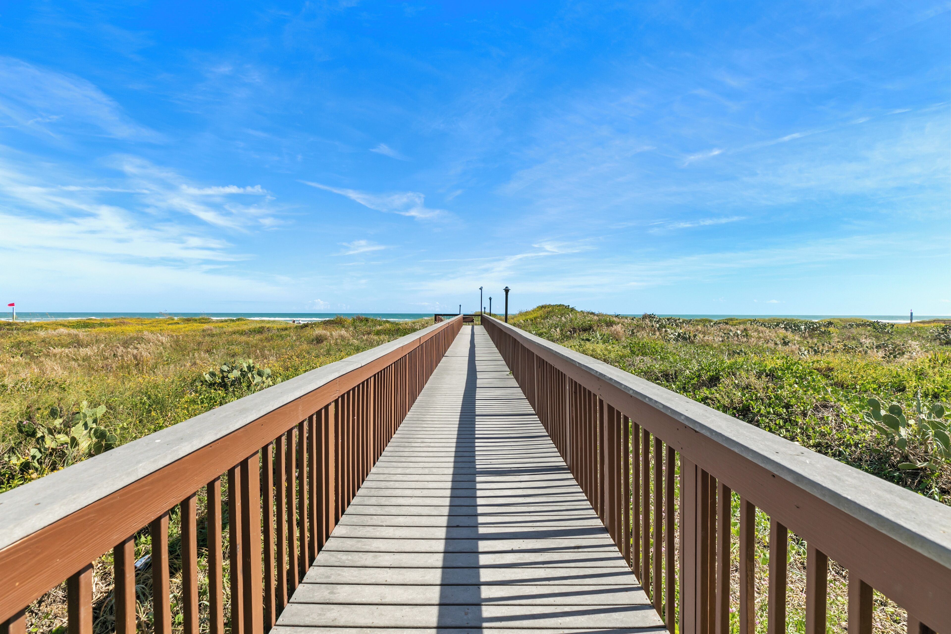 A wooden boardwalk leading to the beach, surrounded by vegetation.