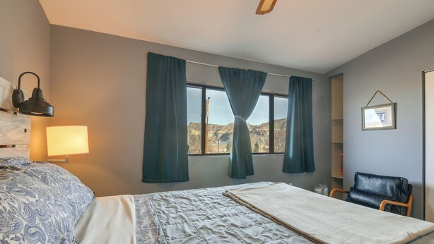 A hotel room with a bed, a desk, a chair, a lamp, and a window with curtains. - Adventure Base 2 Near Lake Powell (Kanab)