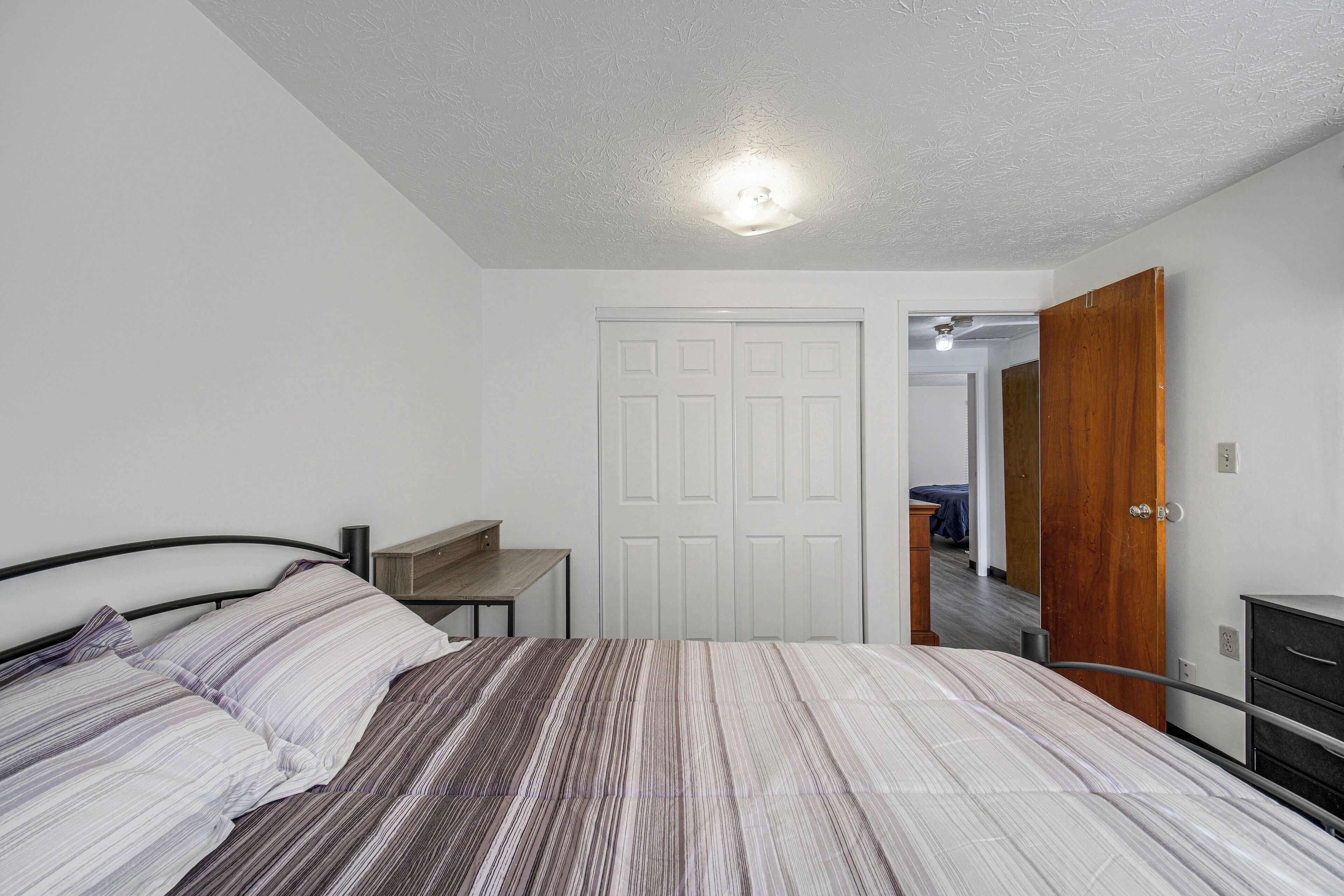 Un dormitorio con cama, escritorio, armario y una puerta que da a otra habitación.