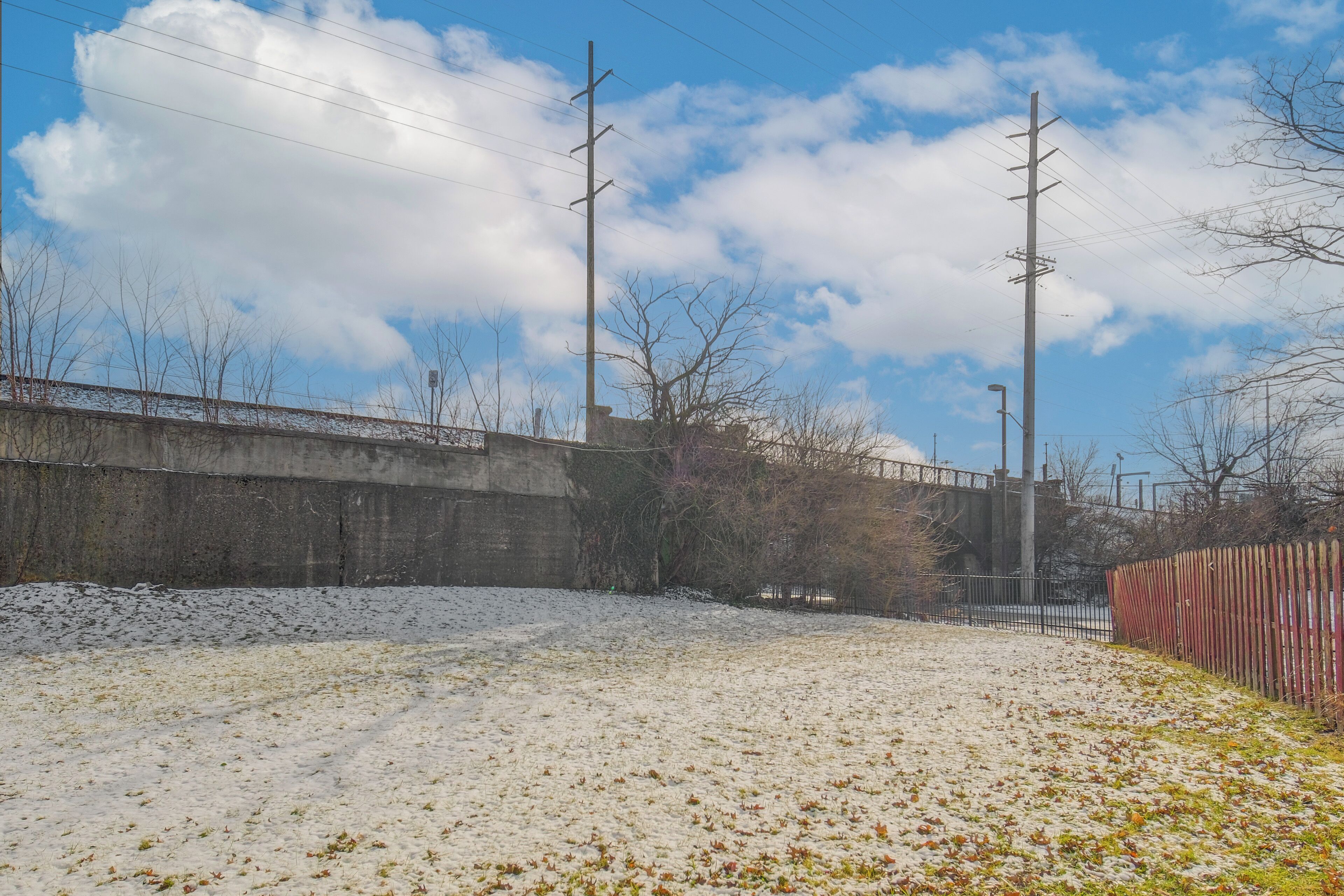 A snowy landscape with a concrete wall, bare trees, and utility poles.