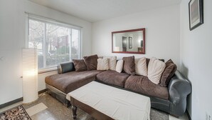 A living room with a sectional sofa, a mirror, and a window with blinds. - Red Line to Airport! Inviting Home in Cleveland (East Cleveland)