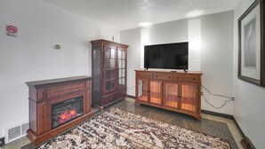 A living room with a fireplace, a television on a wooden cabinet, and a patterned rug. - Red Line to Airport! Inviting Home in Cleveland (East Cleveland)