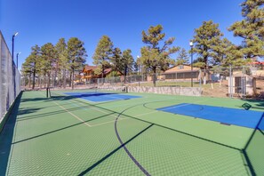 Ein Basketballplatz im Freien mit grüner Spielfläche und blauen Markierungen, umgeben von Bäumen und einem Zaun.