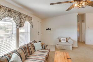 Ein Wohnzimmer mit einem gestreiften Sofa, einem Holztisch, einem weißen Sessel und einem Deckenventilator.
