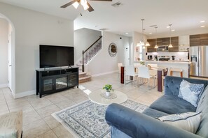 A modern living room with a television, sofa, coffee table, and a staircase leading to a kitchen area. - Golf, Dine & Unwind Poolside! Haines City Getaway (Haines City)